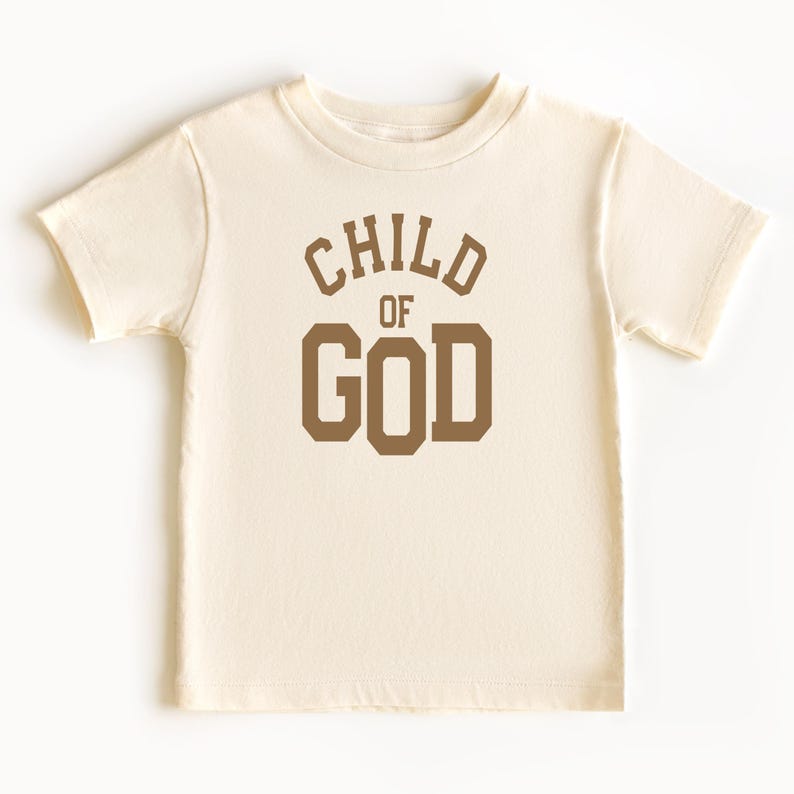 May include: A cream colored short-sleeved t-shirt with the words "CHILD OF GOD" printed in brown on the front.