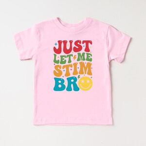 K&ouml;nnte beinhalten: Rosafarbenes T-Shirt f&uuml;r Kleinkinder mit einer Retro-Grafik, auf der "Just Let Me Stim Bro" in bunten Buchstaben mit einem Smiley steht.