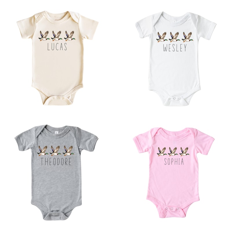May include: Four baby onesies with a line of flying ducks and a name printed below. The onesies are in beige, white, grey, and pink.