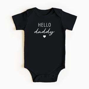 May include: Black baby onesie with white text that says "HELLO daddy" with a small white heart below the text.
