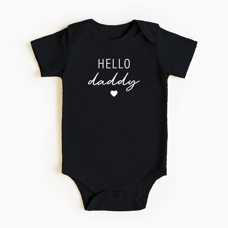 May include: Black baby onesie with white text that says "HELLO daddy" with a small white heart below the text.