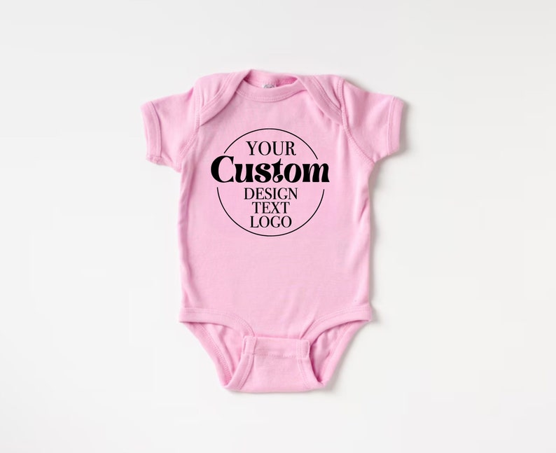 Op de afbeelding: Roze baby onesie met een zwarte cirkel en de tekst "YOUR CUSTOM DESIGN TEXT LOGO" in een retro lettertype.