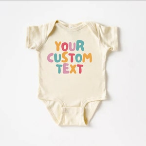 May include: A cream-colored baby onesie with the text "YOUR CUSTOM TEXT" in colorful, bubble-like letters.