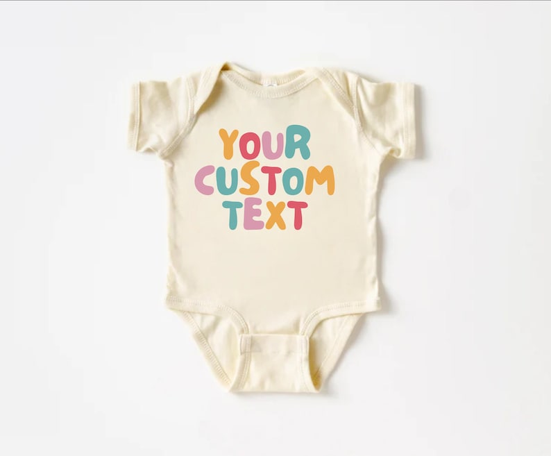 May include: A cream-colored baby onesie with the text "YOUR CUSTOM TEXT" in colorful, bubble-like letters.