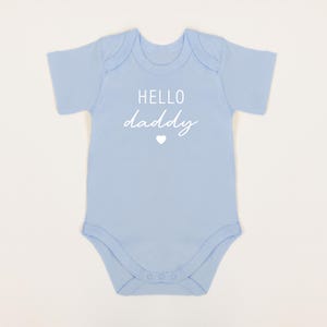 May include: A light blue baby onesie with the text "HELLO daddy" in white with a small white heart.