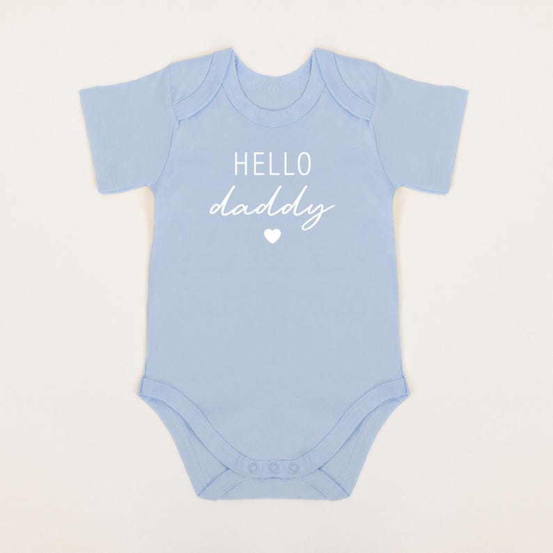 May include: A light blue baby onesie with the text "HELLO daddy" in white with a small white heart.