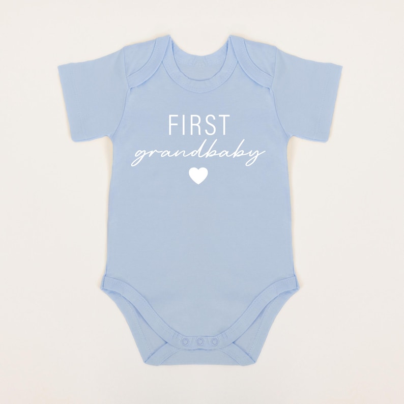 May include: A light blue baby onesie with the text "FIRST grandbaby" in white with a white heart.
