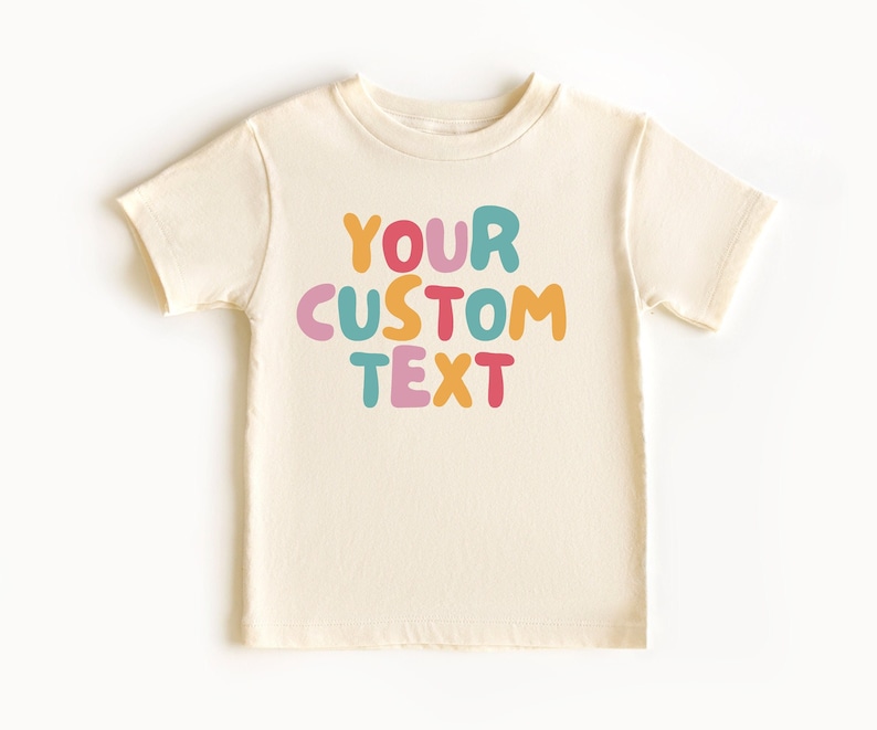 May include: A cream colored t-shirt with the text "YOUR CUSTOM TEXT" in colorful, bubble-like letters.