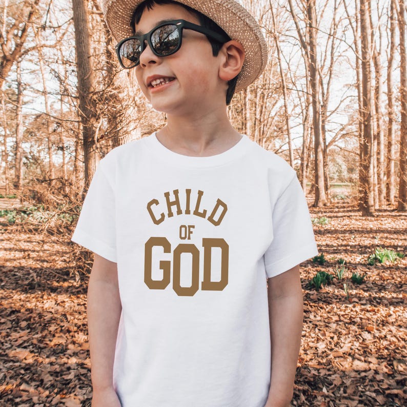 May include: A white t-shirt with a brown graphic that says "CHILD OF GOD" in a bold font.