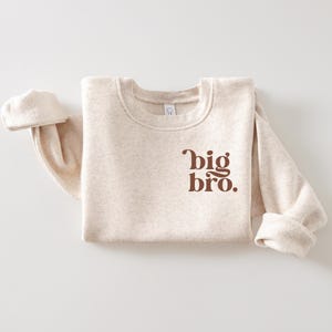 May include: A beige sweatshirt with the text "big bro." printed in brown on the front.