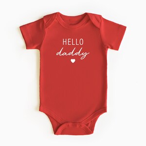 May include: Red baby onesie with white text that says "HELLO daddy" and a small white heart.