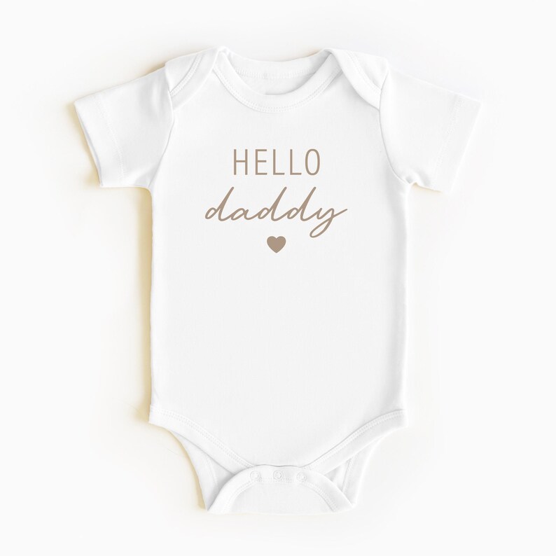 May include: White baby onesie with brown text that says "HELLO daddy" with a small brown heart below the text.