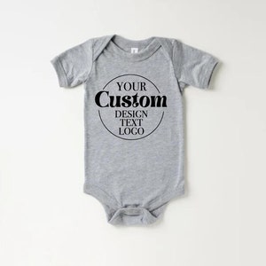 Op de afbeelding: Een grijze baby romper met korte mouwen en een zwarte cirkelvormige afbeelding met de tekst "YOUR CUSTOM DESIGN TEXT LOGO".