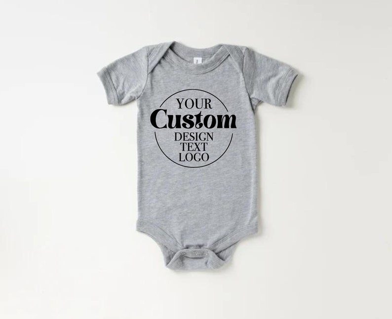 Op de afbeelding: Een grijze baby romper met korte mouwen en een zwarte cirkelvormige afbeelding met de tekst "YOUR CUSTOM DESIGN TEXT LOGO".
