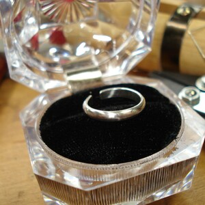 May include: A silver ring in a clear plastic ring box with a black velvet interior.