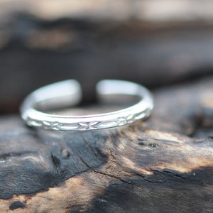 May include: A silver toe ring with a delicate floral design.