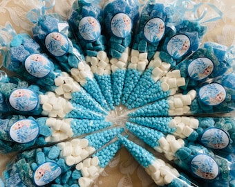 May include: A collection of blue and white party favor cones filled with blue candies, white marshmallows, and blue sprinkles. Each cone has a round sticker with a cartoon image of a girl with blonde hair and a blue dress. The text "Anna and Elsa" is printed on the sticker.