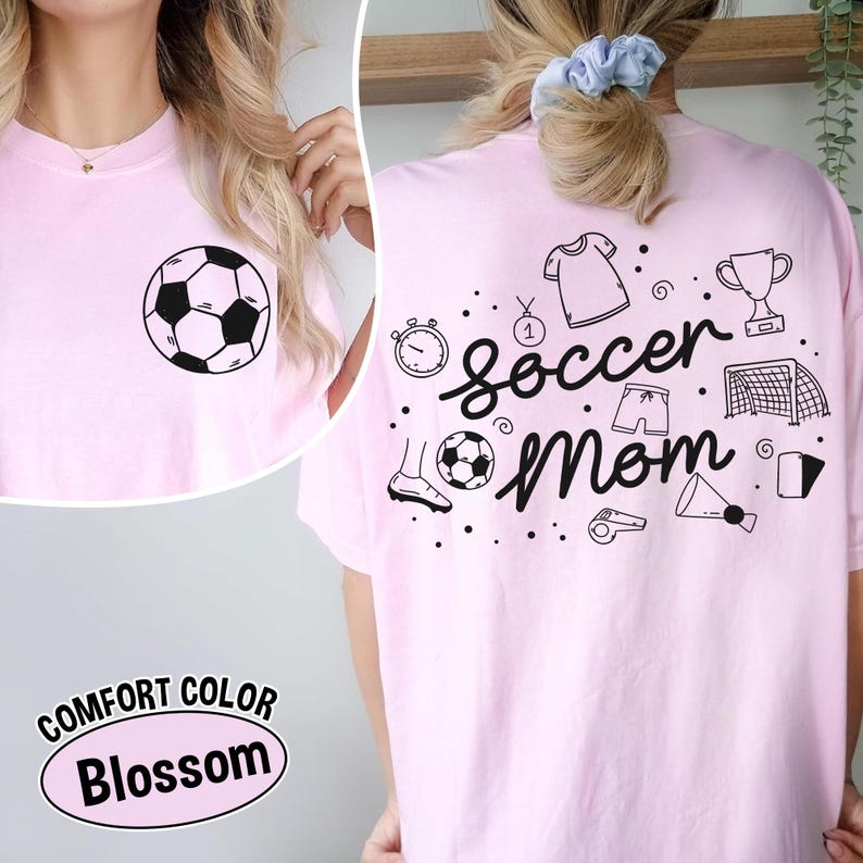 K&ouml;nnte beinhalten: Hellrosa T-Shirt mit einem schwarz-wei&szlig;en Fu&szlig;ball-Grafik auf der Vorderseite. Auf der R&uuml;ckseite des Shirts steht "Soccer Mom" mit Fu&szlig;ball-Themen-Kritzeleien. Das Shirt ist mit "Comfort Color Blossom" gekennzeichnet.