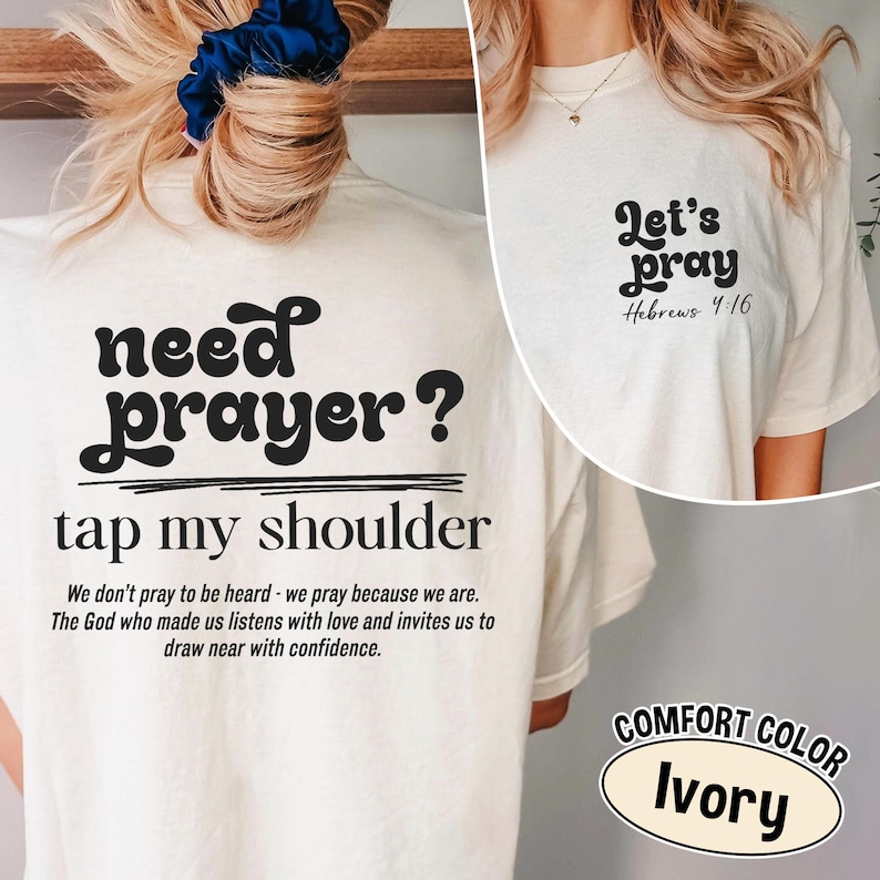 K&ouml;nnte beinhalten: Elfenbeinfarbenes T-Shirt mit dem schwarzen Text "need prayer? tap my shoulder". Auf der R&uuml;ckseite steht eine Botschaft &uuml;ber das Gebet. Auf der Vorderseite steht "Let's pray Hebrews 4:16".