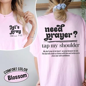 K&ouml;nnte beinhalten: Hellrosa T-Shirt mit den Aufdrucken "Let's pray" und "Hebrews 4:16" auf der Vorderseite. Auf der R&uuml;ckseite des Shirts steht "need prayer? tap my shoulder" mit einer Botschaft. Das Shirt ist Comfort Color Blossom.