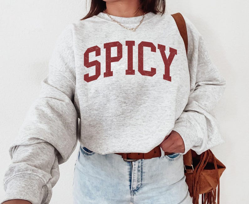 May include: A gray sweatshirt with the word "SPICY" printed in red on the front. The sweatshirt has a relaxed fit and long sleeves.