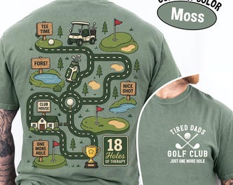 May include: Moss green t-shirt with a golf course design. The back features a road map with golf-related illustrations and text, including "TEE TIME," "FORE!," and "18 Holes of Therapy." The front has the text "TIRED DADS GOLF CLUB."