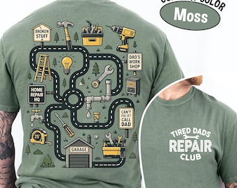 May include: A moss green t-shirt with a graphic of a road map with tools and the text "BROKEN STUFF", "HOME REPAIR HQ", "DAD'S WORK SHOP", "GARAGE", and "CAN'T FIX IT? CALL DAD". The shirt also features the text "TIRED DADS REPAIR CLUB".