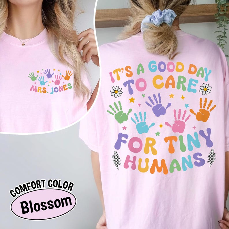 Puede incluir: Camiseta rosa claro con huellas de manos coloridas y el texto "MRS. JONES" en la parte delantera. La parte trasera de la camiseta muestra la frase "IT'S A GOOD DAY TO CARE FOR TINY HUMANS" en colores arco&iacute;ris.