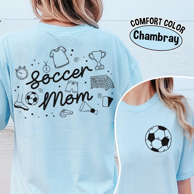 K&ouml;nnte beinhalten: Hellblaues T-Shirt mit dem Schriftzug "Soccer Mom" und Fu&szlig;ball-Grafiken in Schwarz. Das Shirt hat auch den Text "Comfort Color Chambray" in einem wei&szlig;en Oval.