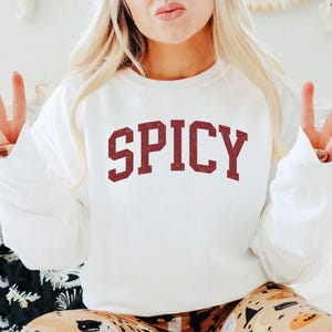 May include: White sweatshirt with the word "SPICY" printed in red on the front.