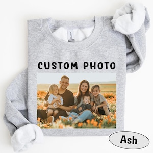 May include: Light gray sweatshirt with a family photo and the text "CUSTOM PHOTO" in black. The photo shows a family of five sitting in a field of orange flowers. The word "Ash" is in a gray oval.