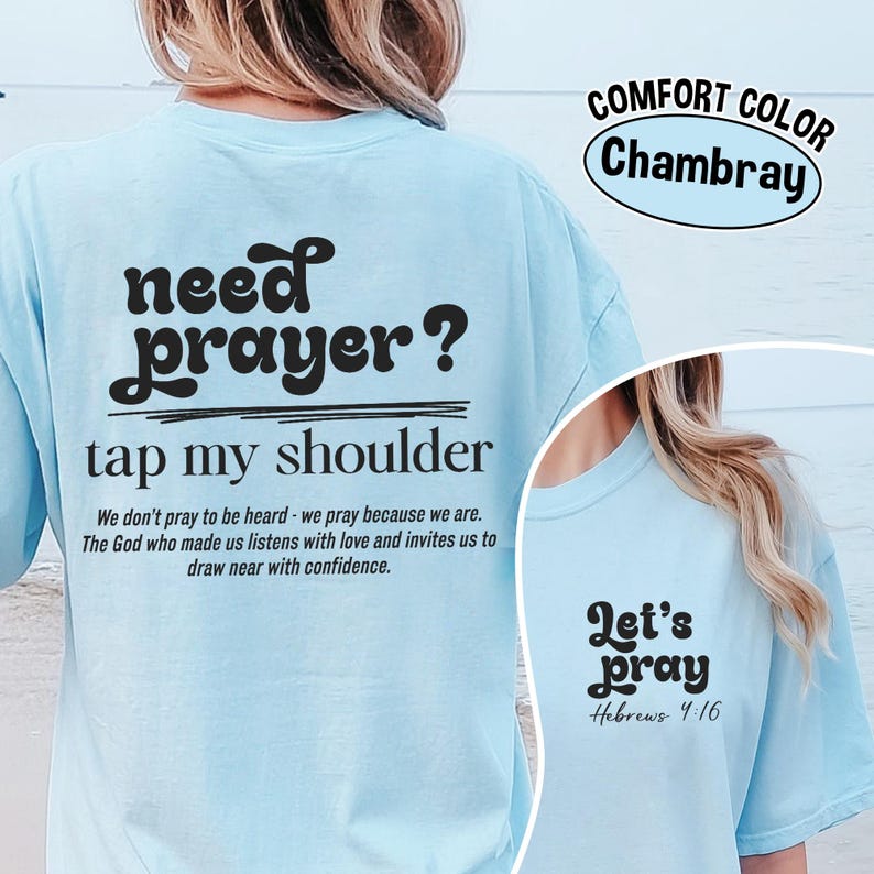 K&ouml;nnte beinhalten: Hellblaues T-Shirt mit dem Text "need prayer? tap my shoulder" in Schwarz. Das Shirt hat auch den Text "Let's pray Hebrews 4:16". Das T-Shirt besteht aus Comfort Color Chambray-Material.