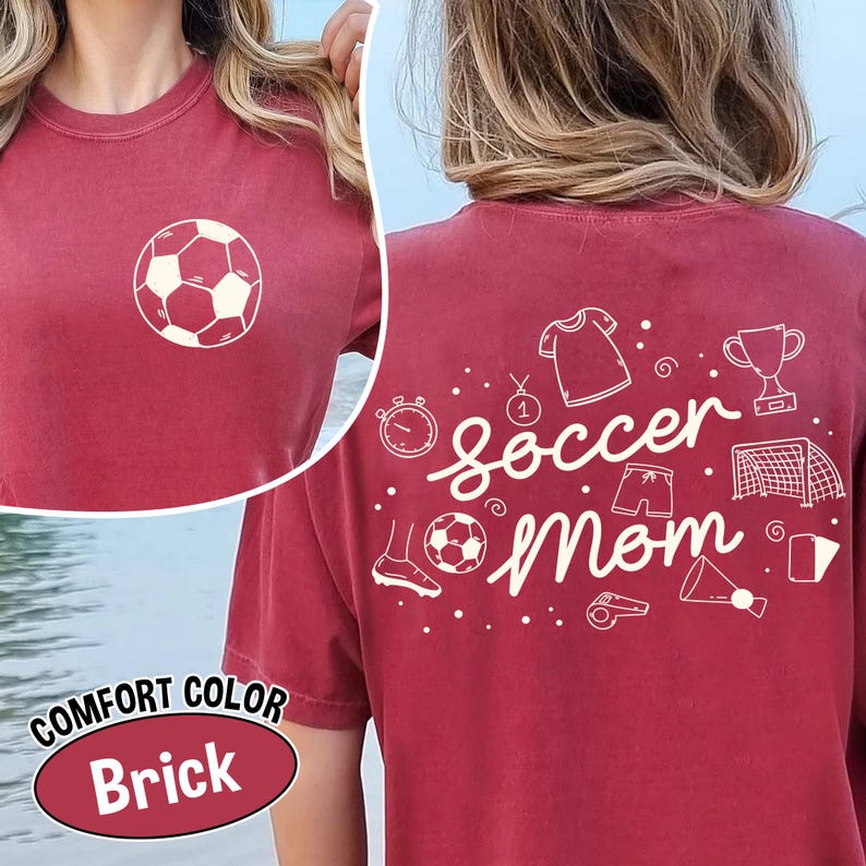 K&ouml;nnte beinhalten: Ziegelrotes T-Shirt mit einem Fu&szlig;ball-Motiv auf der Vorderseite. Auf der R&uuml;ckseite des Shirts steht "soccer mom" mit Illustrationen zum Thema Fu&szlig;ball. Das Shirt ist mit "Comfort Color" gekennzeichnet.