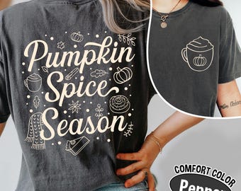 May include: A dark gray t-shirt with the words "Pumpkin Spice Season" in a cream-colored script, along with fall-themed illustrations. A smaller image of a coffee cup with a pumpkin is on the front. The shirt is labeled "Comfort Color Pepper".