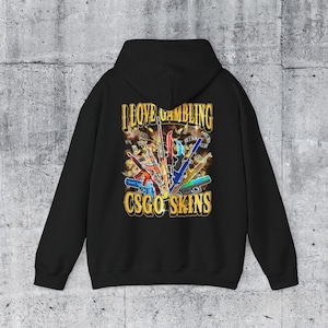 May include: Black hoodie with a graphic design on the back. The design features various colorful guns, money, and the text "I LOVE GAMBLING CSGO SKINS" in gold lettering.