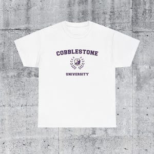 May include: White t-shirt with a purple print that says "Cobblestone University" with a crest and laurel wreath.