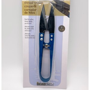 May include: A pair of blue and black thread snips with metal blades, packaged on a white cardboard backing labeled BASIC elements and THE BEADSMITH. The packaging includes text in English, French, and Spanish regarding the tool's function.