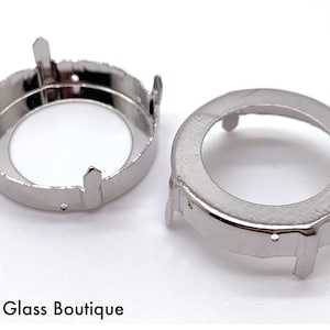 May include: Two silver metal settings for a bezel setting. The settings have four prongs and a round opening.