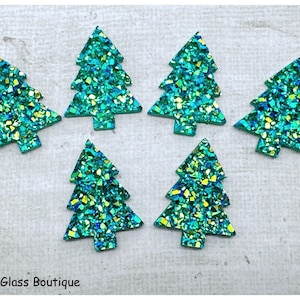 May include: Six flat, triangular Christmas tree-shaped embellishments featuring a vibrant green and blue glitter finish with reflective, multi-colored flecks. The text "Bead & Glass Boutique" is printed in black in the bottom left corner.