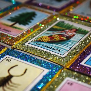 May include: A set of colorful playing cards with glitter borders. The cards feature images of a pine tree, a boat, a scorpion, and a crown. The text on the cards includes "El Pino", "La Chalupa", and "La Corona".