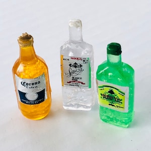 May include: Three miniature glass bottles with labels. The bottle on the left is yellow and says "Corona Extra". The bottle in the middle is clear and says "Sauza Blanco Tequila". The bottle on the right is green and says "Horchitos".