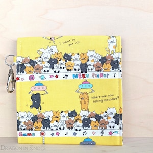 May include: Yellow fabric wallet with a cat-themed design. The wallet features rows of cartoon cats, UFOs, and text that reads "I want to get it!!" and "Where are you taking me today?" Includes a silver-colored key ring.