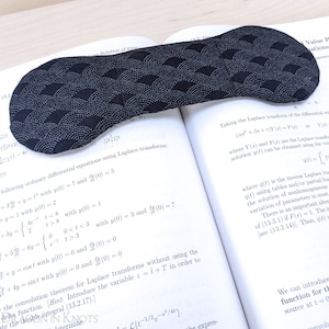 May include: A black eye mask with a white wave pattern. The mask is made of fabric and has a soft, comfortable feel. It is perfect for blocking out light and promoting relaxation.