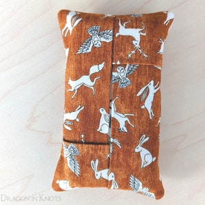 Peut inclure: Un couvre-boîte à mouchoirs brun avec un imprimé d'animaux de la forêt en blanc et brun. Le couvre-boîte représente des hiboux, des cerfs, des renards et des lapins.