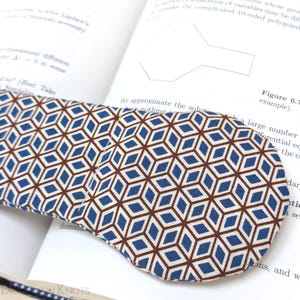 May include: A blue and brown geometric patterned bookmark with a white background. The bookmark is folded over a book.