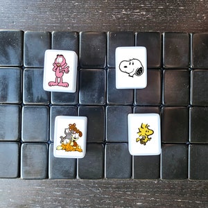 May include: A black and white game board with four white tiles. Each tile features a cartoon character. One tile has a pink cat, one has a black and white dog, one has a yellow bird, and one has a white dog.