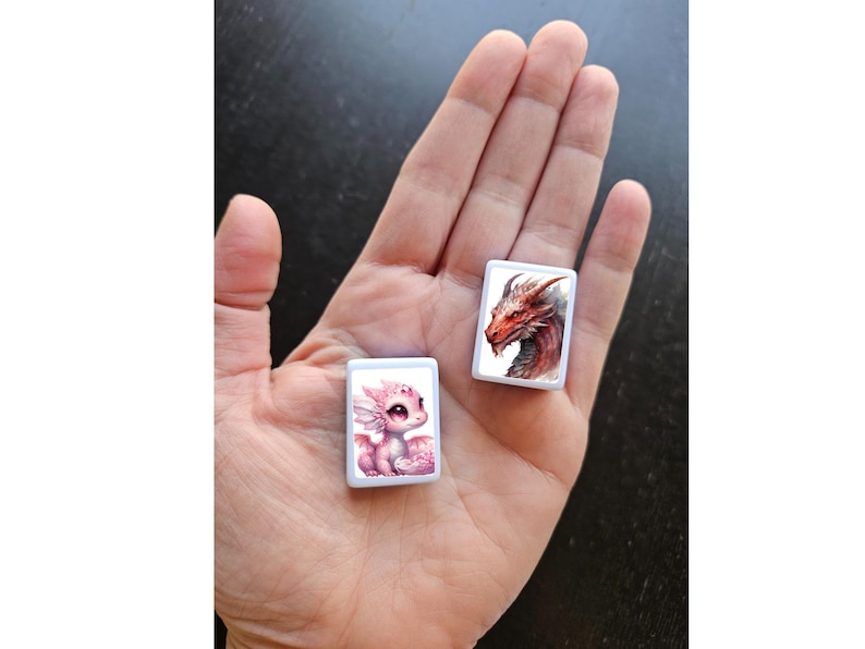 May include: Two small white square tiles with images of dragons. The tile on the left features a pink dragon with wings and the tile on the right features a red dragon with wings.