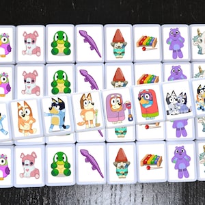 K&ouml;nnte beinhalten: Ein Satz von 18 passenden Kacheln mit verschiedenen Comicfiguren, darunter eine lila Eule, ein rosa Welpe, ein gr&uuml;ner Frosch, ein lila Monster, ein Einhorn und ein blauer Hund. Die Kacheln sind wei&szlig; mit abgerundeten Kanten und in einem Raster angeordnet.