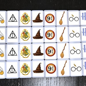 May include: A set of 16 white square tiles with various Harry Potter themed images. The images include the Hogwarts crest, a Sorting Hat, a broomstick, a lightning bolt, a pair of glasses, and the number "9 3/4".