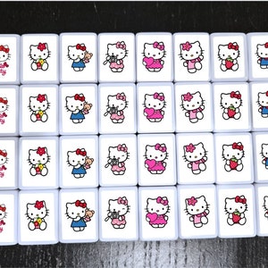 May include: A set of 16 white ceramic tiles with Hello Kitty images. Each tile features a different Hello Kitty design, including Hello Kitty holding a camera, a heart, a strawberry, and a teddy bear. The tiles are perfect for playing games or decorating a room.